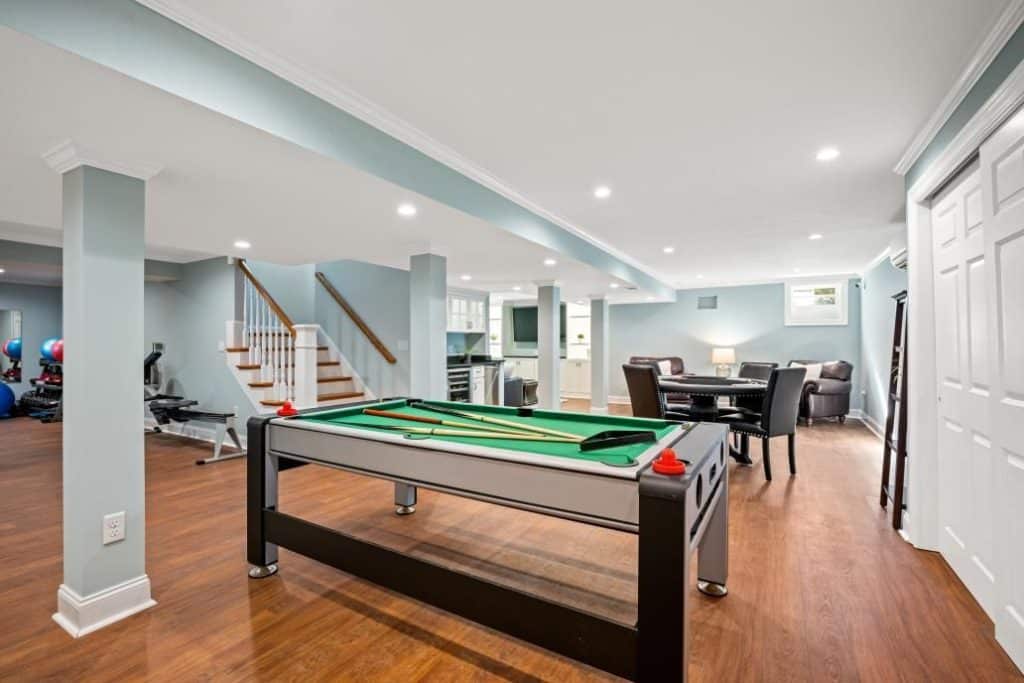 basement of home with light blue paint, pool table in middle, exercise equipment in back